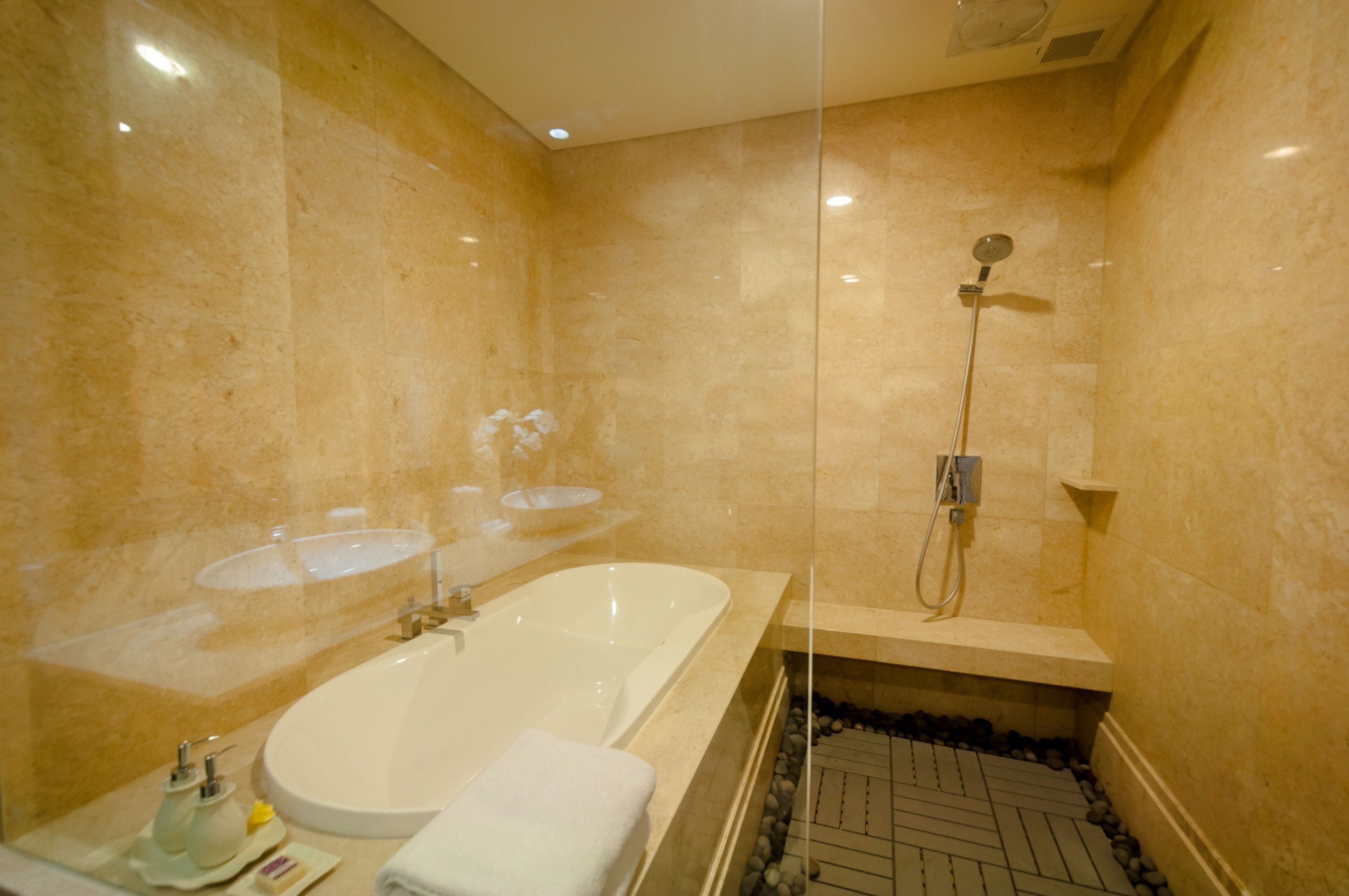 Een moderne badkamer met een ruime badkuip, een douche met glazen wand en een betegelde muur van marmer.