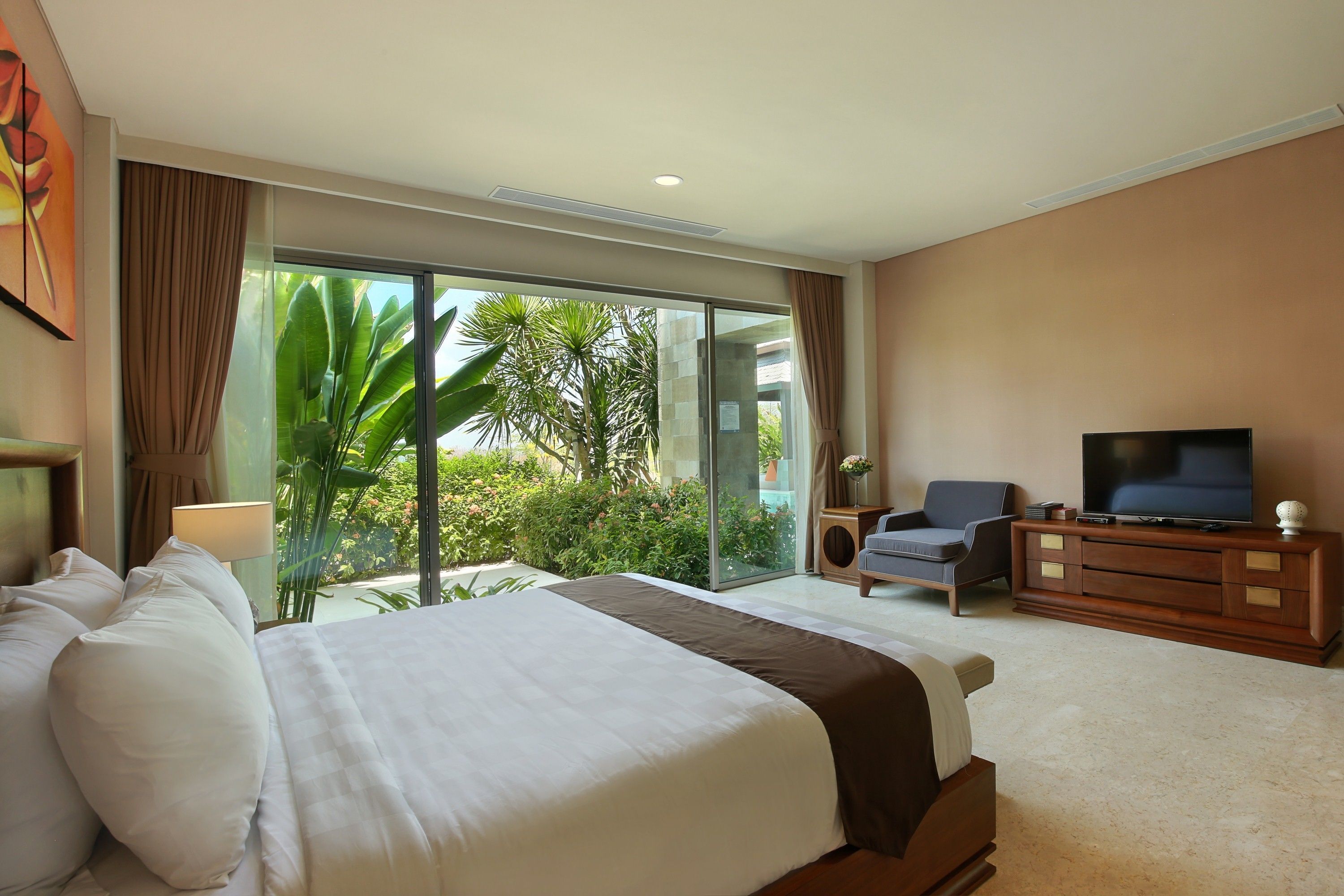 Habitación de hotel con una cama grande, televisión, zona de estar y vistas a zonas verdes.