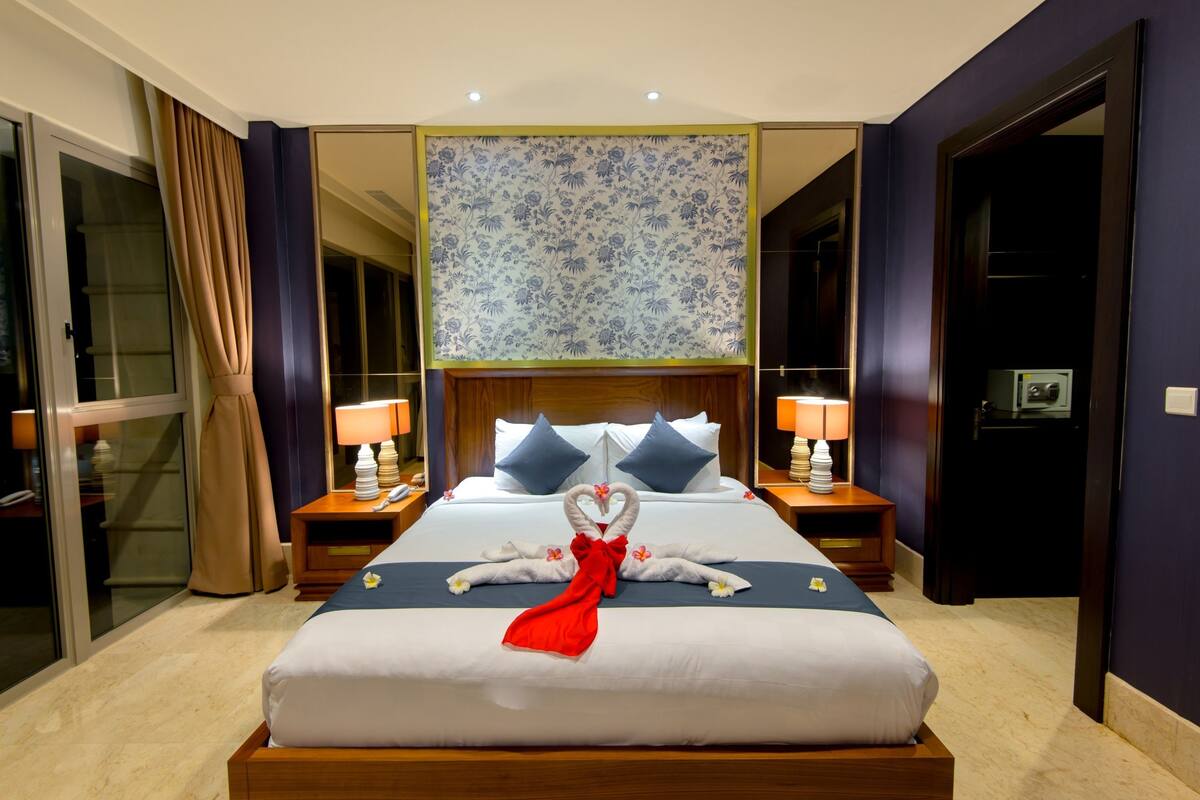 Une chambre d’hôtel avec un grand lit, deux tables de chevet, un miroir et un papier peint à motifs floraux.