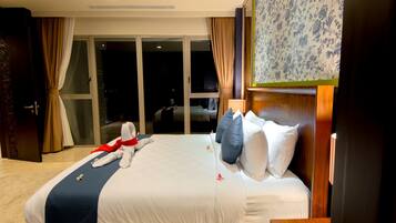 A hotel room with a large bed, a wooden headboard, a nightstand, and a view of the outside through a sliding glass door.