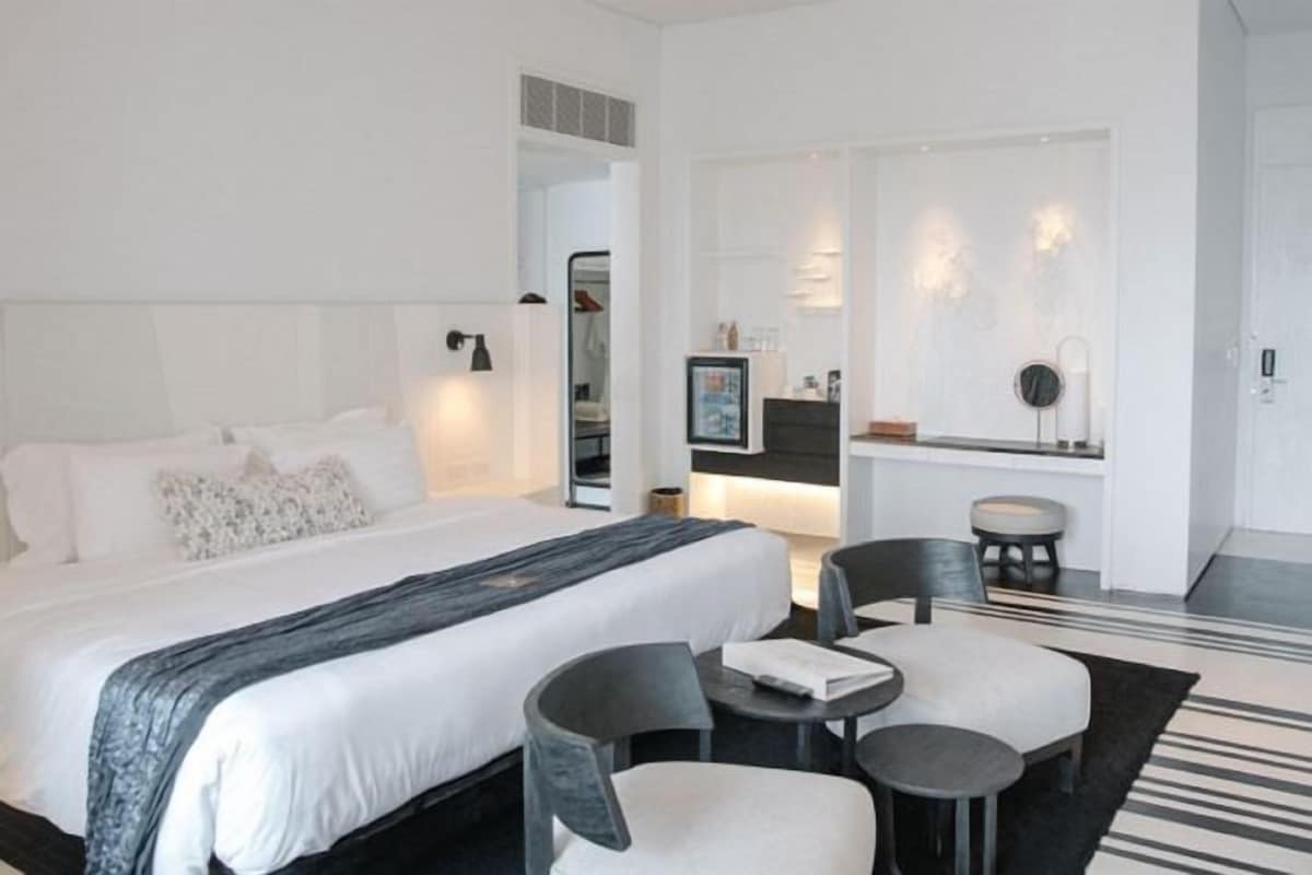 A modern hotel room with a large bed, two chairs, a small table, and a TV.