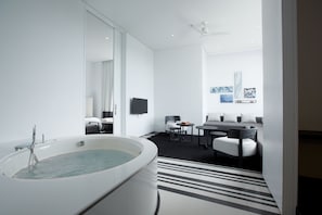 Un baño moderno con una bañera grande, un espejo, un televisor de pantalla plana y una zona de estar con sofá y sillones.