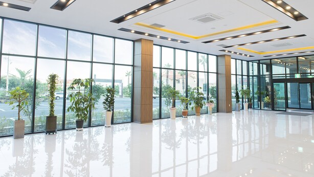 Een ruime lobby met grote ramen, plantenpotten en moderne verlichtingsarmaturen.