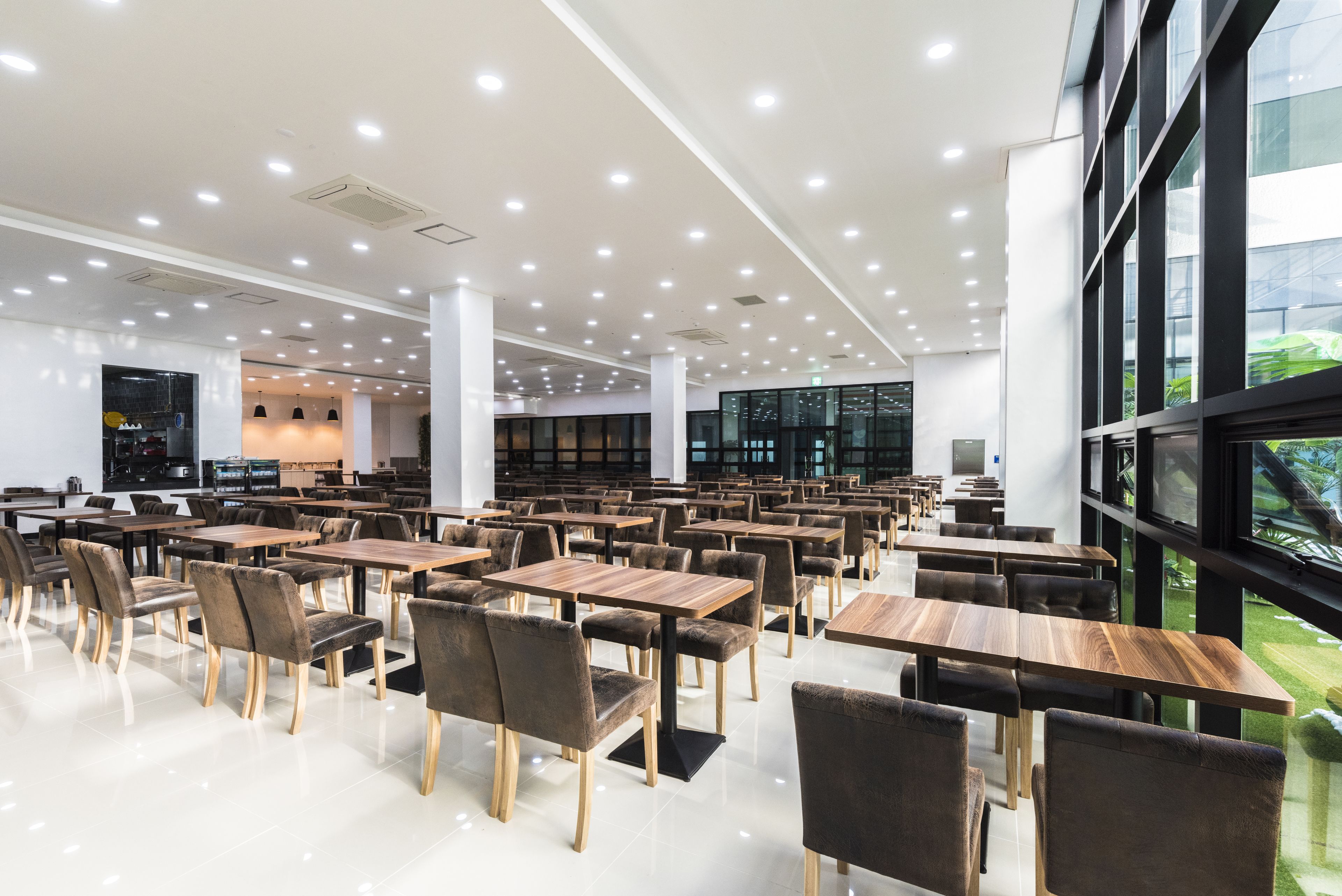 A spacious dining area with multiple tables and chairs, large windows, and a modern ceiling design.