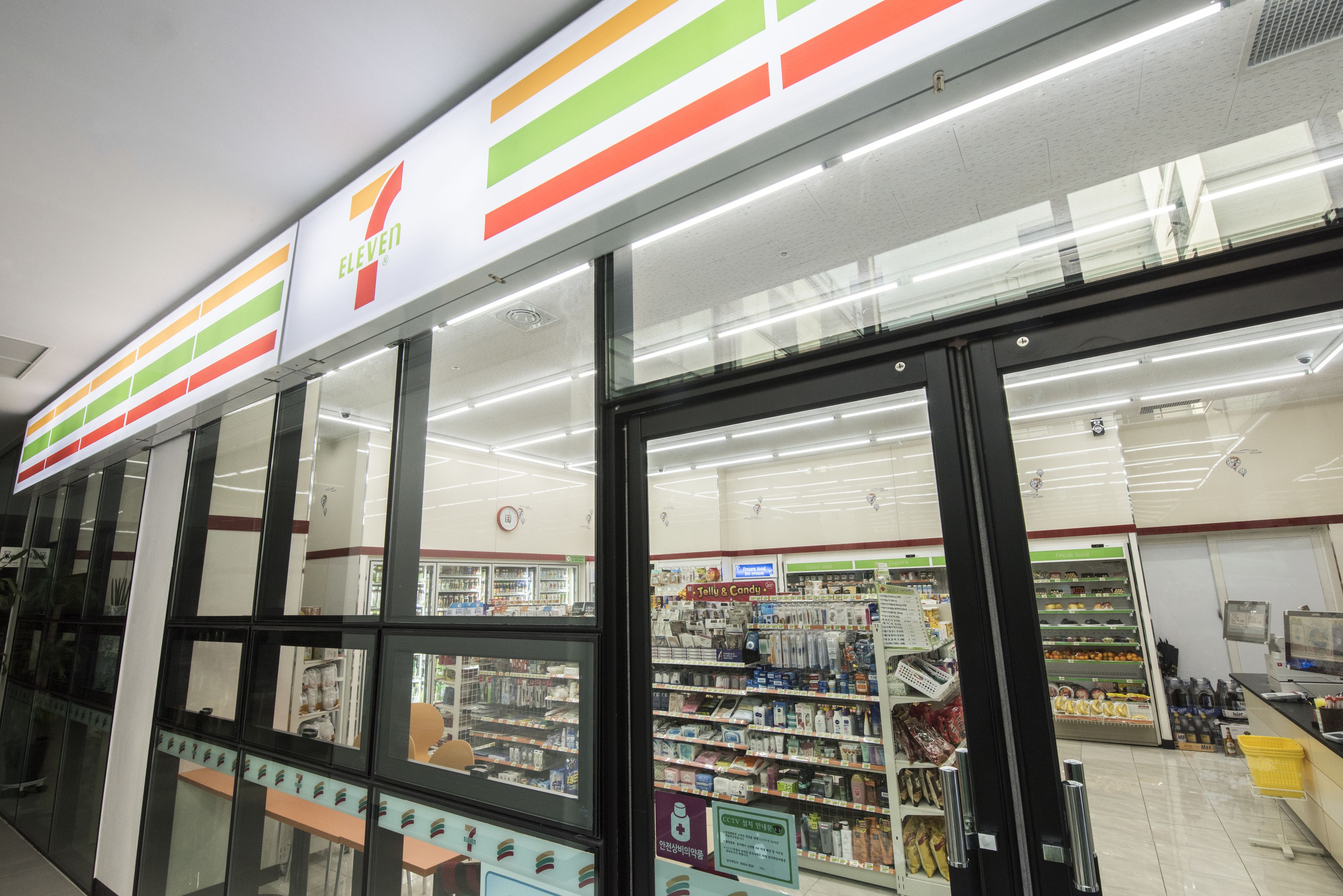 Un magasin 7-Eleven dont l’entrée est bien visible, avec des étagères remplies de divers produits et une zone de caisse clairement identifiable.