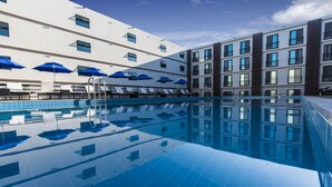 Een modern hotel met een zwembad, meerdere balkons en blauwe parasols.