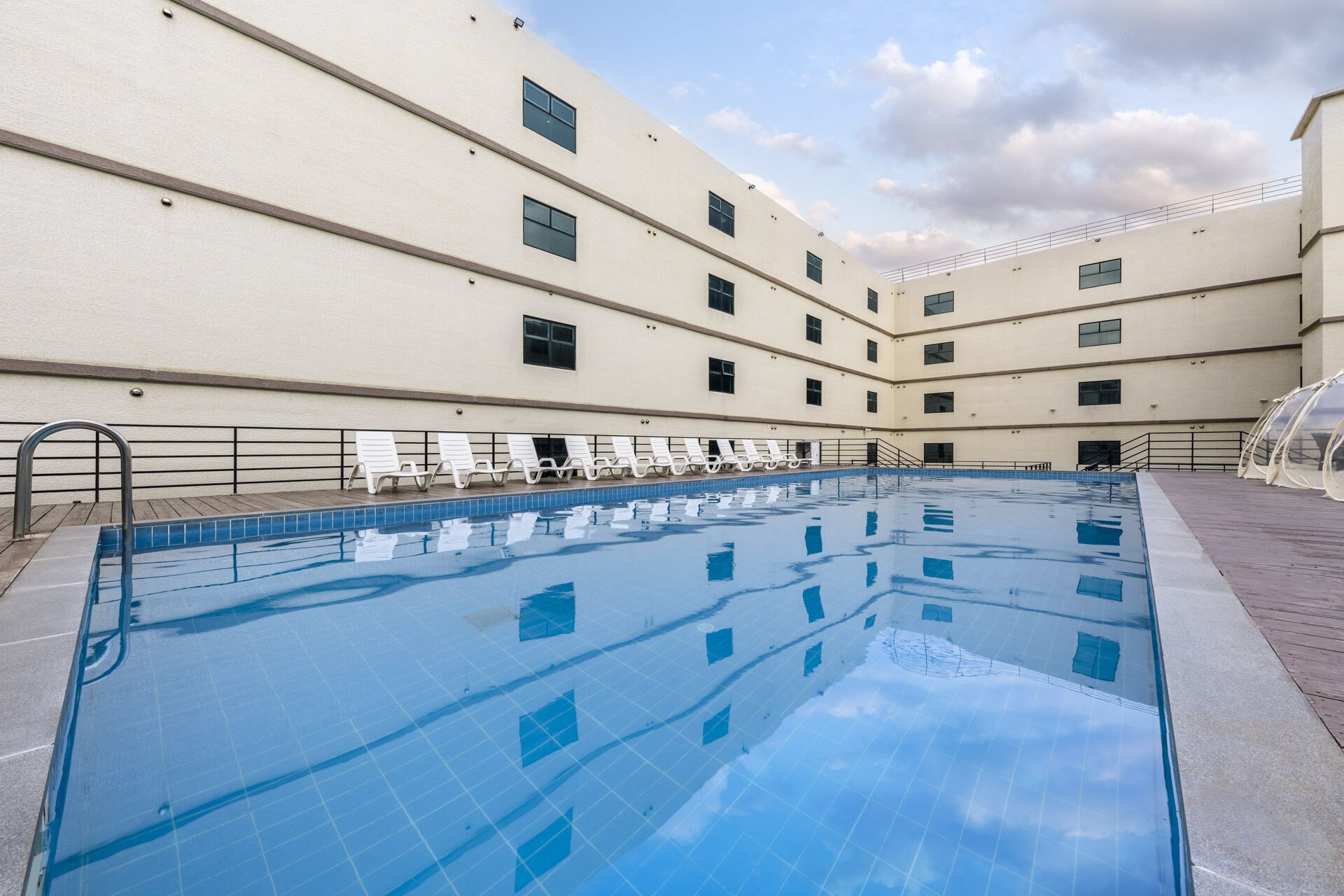 A swimming pool with lounge chairs and a building with multiple windows.