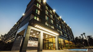 Een modern hotel met een opvallende ingang, meerdere verdiepingen en een zwembad in de voorgrond.