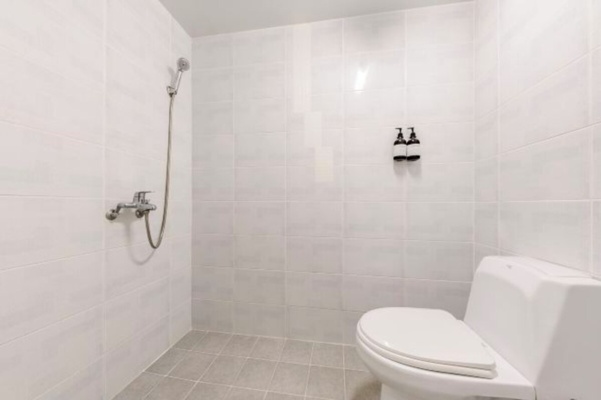 Een kleine, moderne badkamer met witte tegels, een toilet, een douche en een kraan.