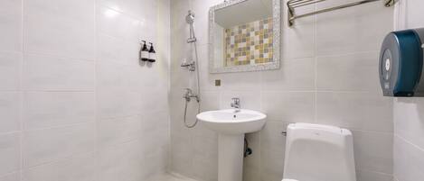 A bathroom with white tiles, a pedestal sink, a toilet, a shower with a handheld showerhead, and a towel rack.