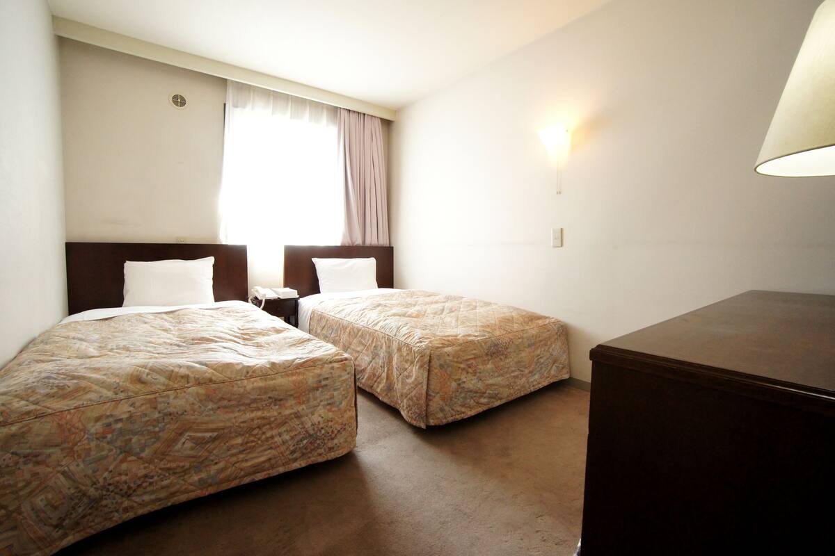 A hotel room with two beds, a nightstand, a lamp, and a dresser.