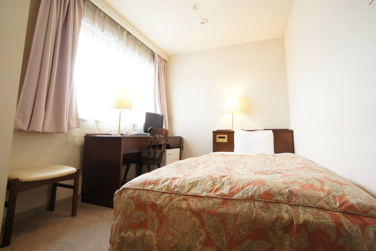 A hotel room with a bed, a desk, a chair, a computer, and two bedside lamps.