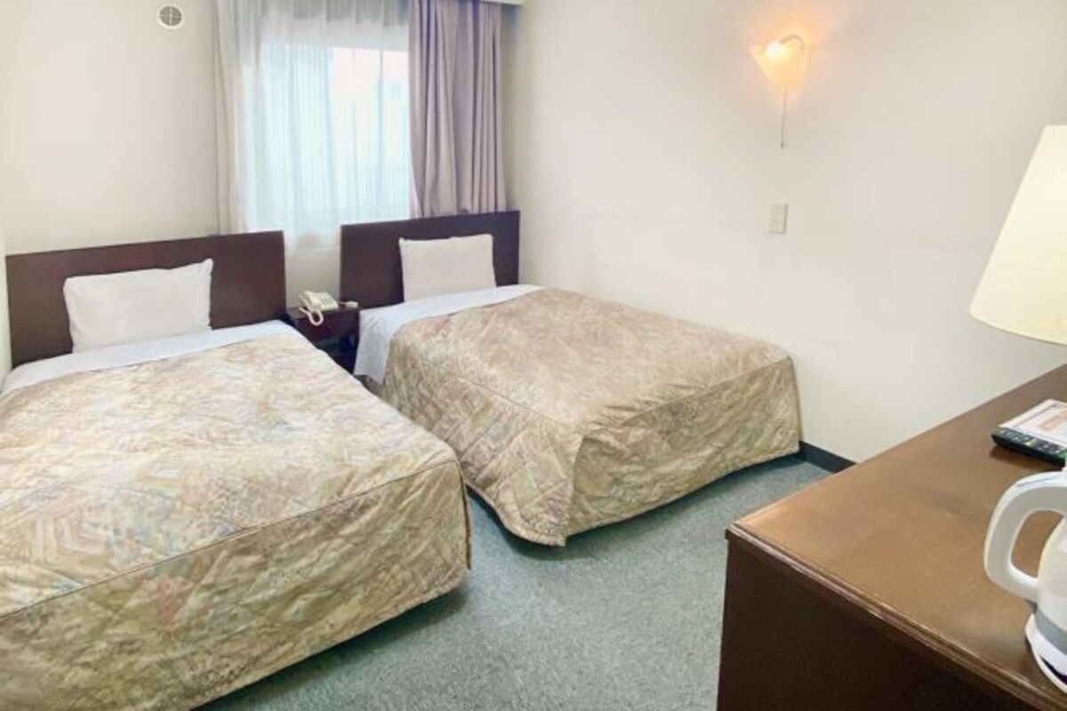 Une chambre d’hôtel avec deux lits, un bureau, une chaise, une lampe et un téléphone.