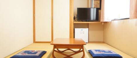 Una habitación japonesa tradicional con suelo de tatami, una mesa de madera baja, un televisor en un estante y una puerta corredera.