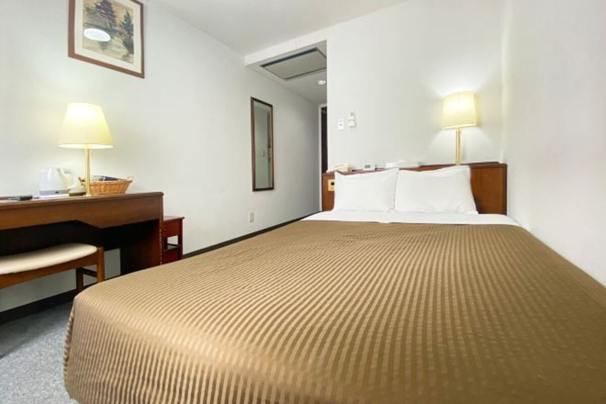 Une chambre d’hôtel avec un lit, un bureau, une chaise et deux lampes.