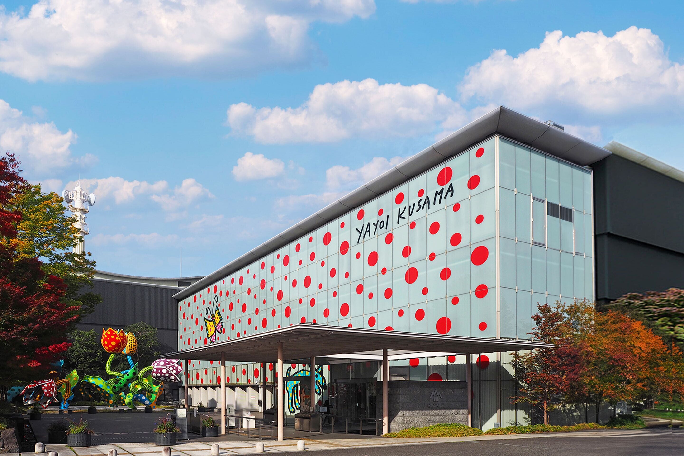 A building with a modern design featuring a glass facade with red circular patterns and the name "Yayoi Kusama" on the side.