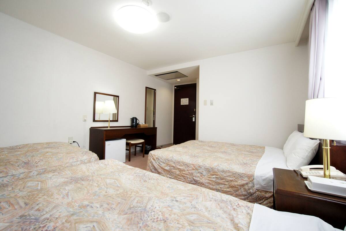 A hotel room with two beds, a desk, a chair, a lamp, and a telephone.