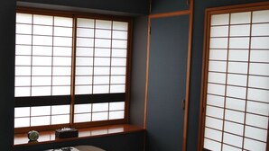 Perinteinen japanilainen huone, jossa on tatamimatto, tummanruskea- ja valkoisilla kuvioilla varustettu peitto sängyllä, shoji-tyyppinen liukuovi ja riippuva paperilyhty.
