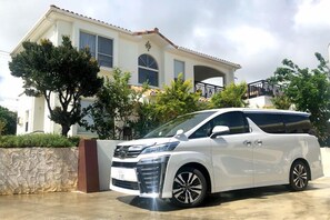 Un fourgonnette blanche était garée devant une maison à deux étages, dotée d’un mur en pierre et d’un balcon.