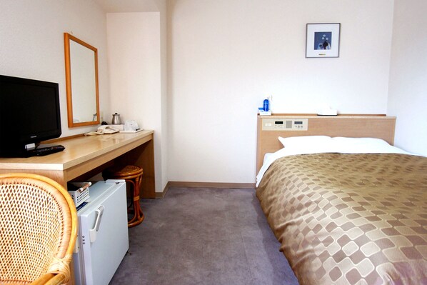 A hotel room with a bed, a desk with a television, a refrigerator, and a wicker chair.