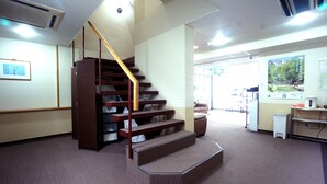 Una escalera con barandilla de madera que lleva a un rellano, suelo alfombrado y vistas a un pasillo con una puerta y un cartel en la pared.