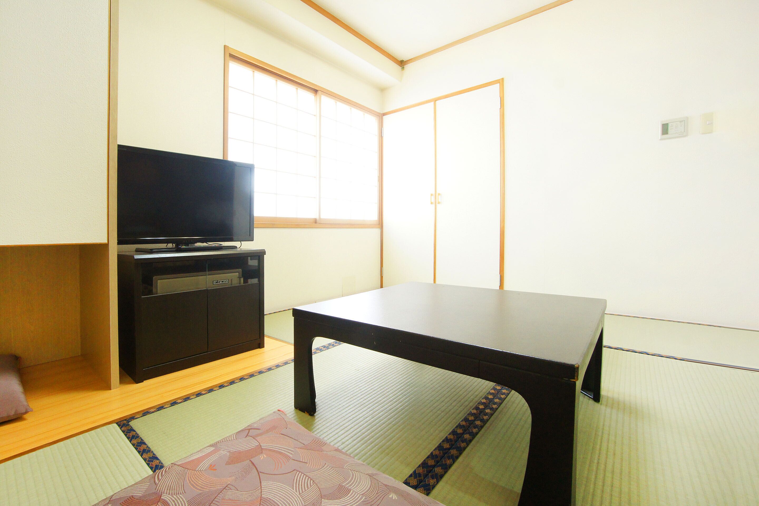 Una habitación con suelo de tatami, televisor en un mueble, una mesa y puertas correderas.