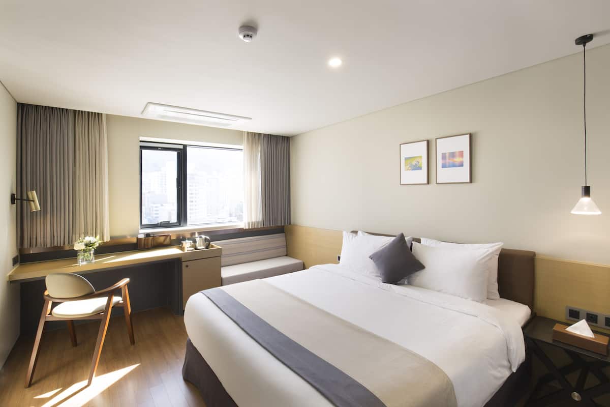 A hotel room with a bed, desk, chair, and a window with curtains.