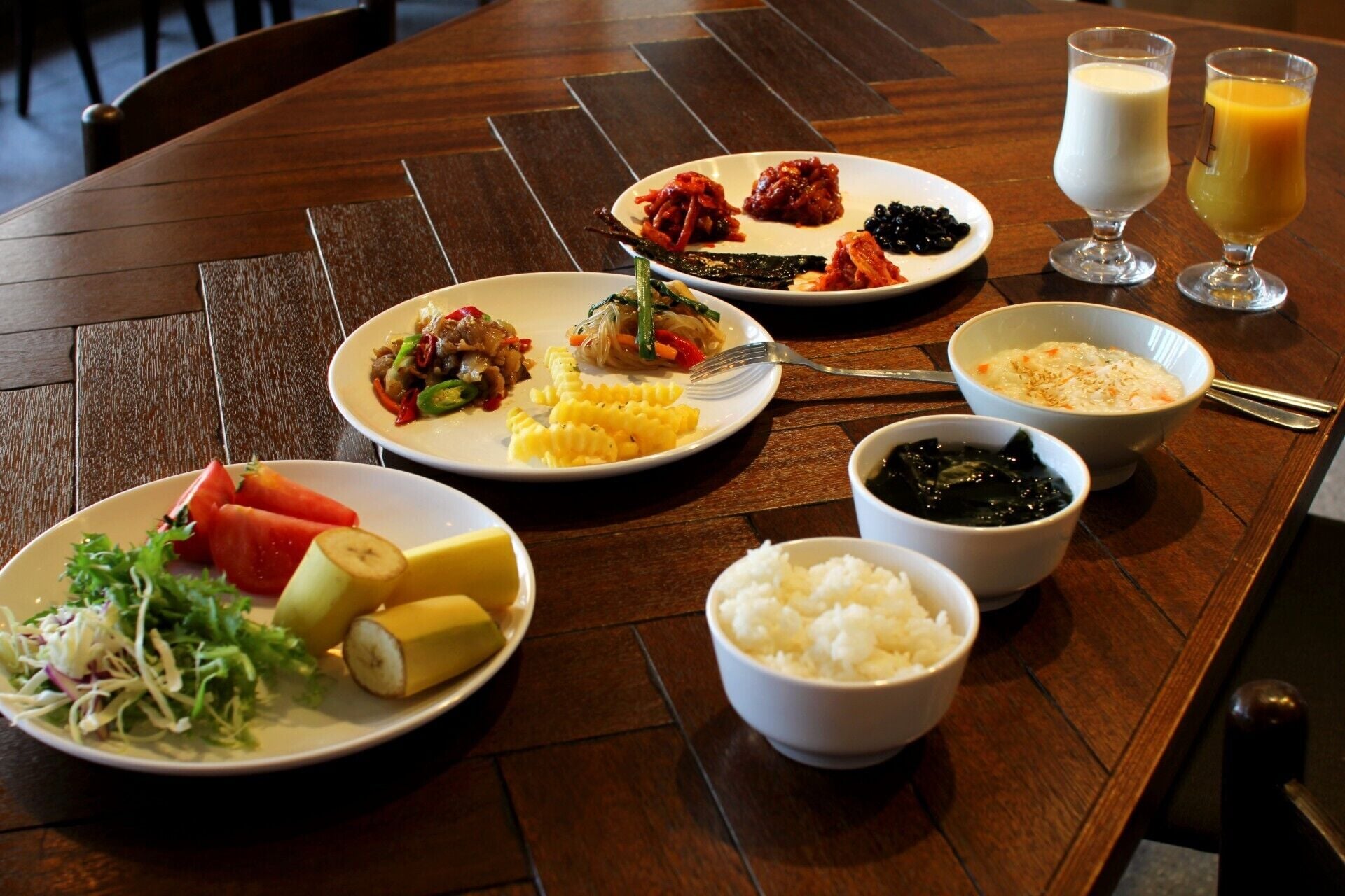 A table with various dishes including rice, vegetables, and a dessert, along with two glasses of orange juice.