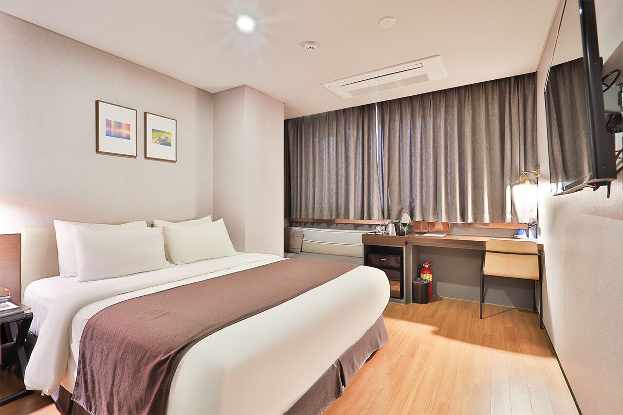 A hotel room with a bed, desk, and a large window with curtains.