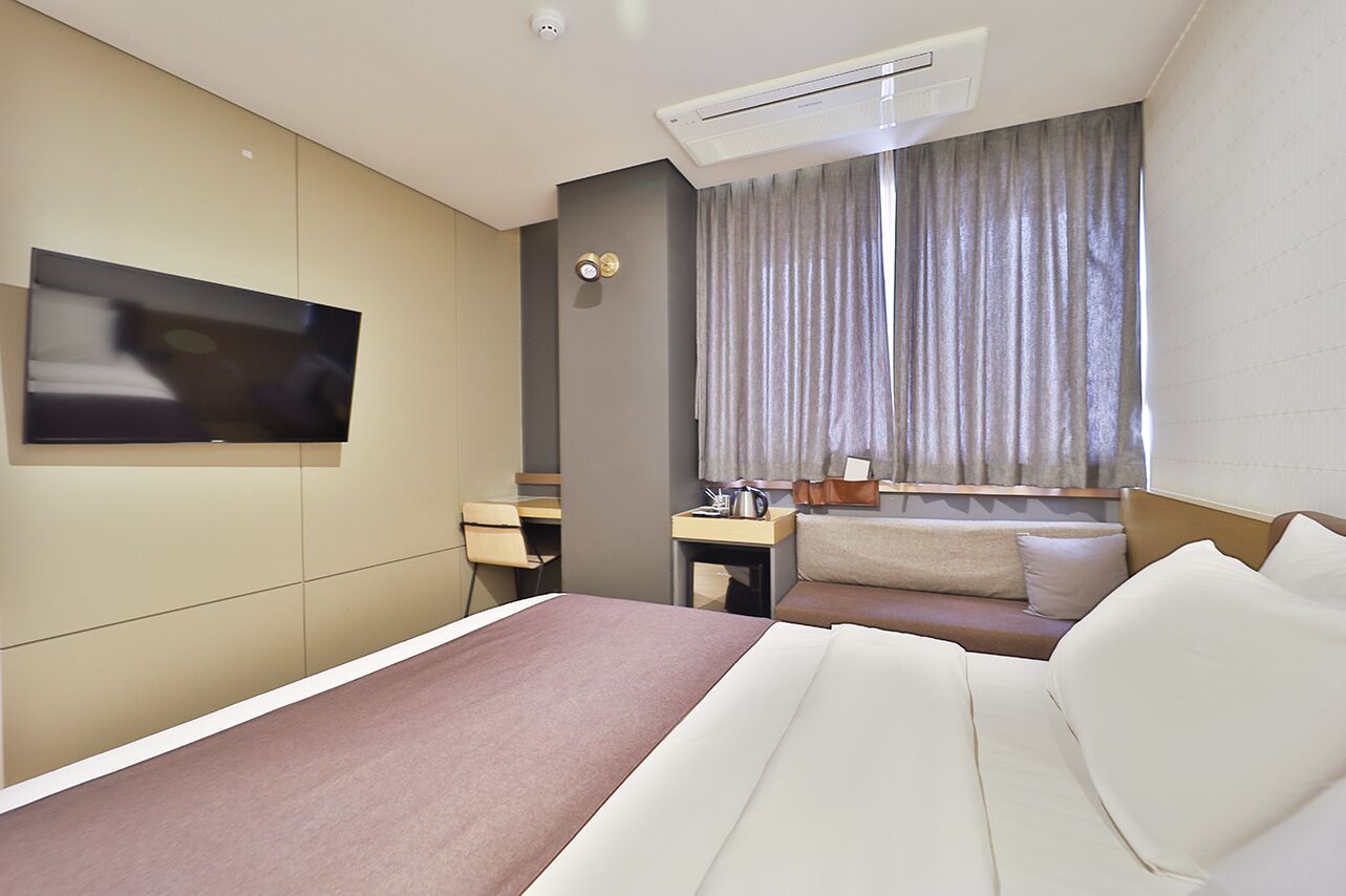 A hotel room with a bed, a desk, a chair, a television, and a window with curtains.