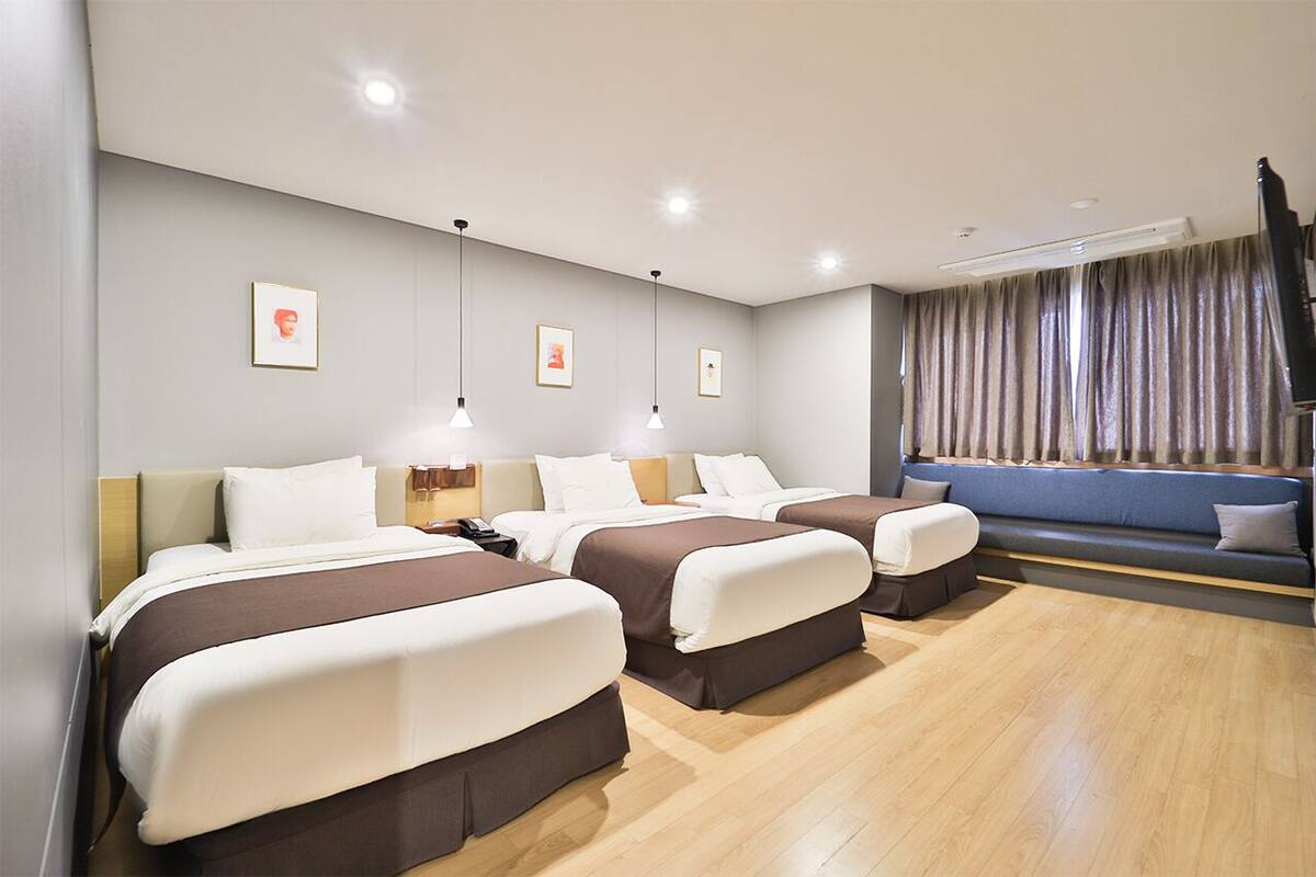 A hotel room with three beds, a sofa, a desk, and a large window with curtains.