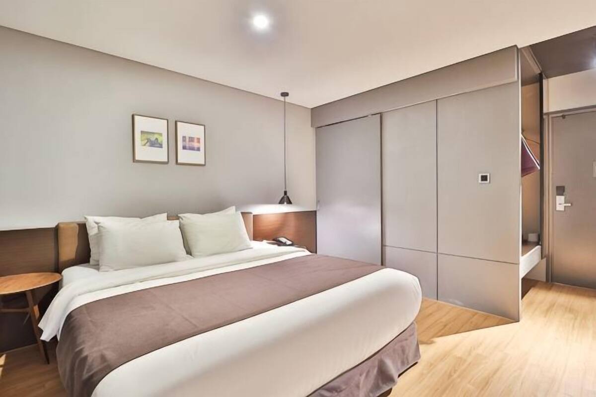 A modern hotel room with a large bed, bedside tables, a wardrobe, and a hanging light fixture.