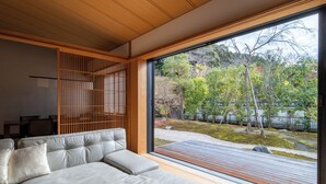 A modern living room with a large window, a sofa, and a wooden partition. - Machiya AOI KYOTO STAY AOI Suites at Nanzenji (Kyoto)