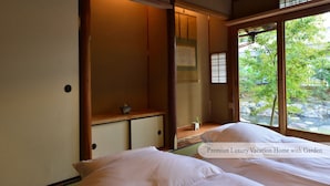 A traditional Japanese-style bedroom with tatami flooring, a wooden bed frame, and a view of a garden through large windows. - Machiya AOI KYOTO STAY AOI Suites at Nanzenji (Kyoto)