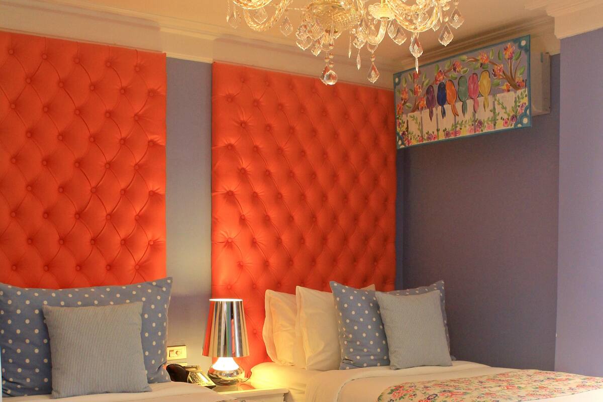 A double bed with a floral bedspread and a tufted headboard in a room with a chandelier.