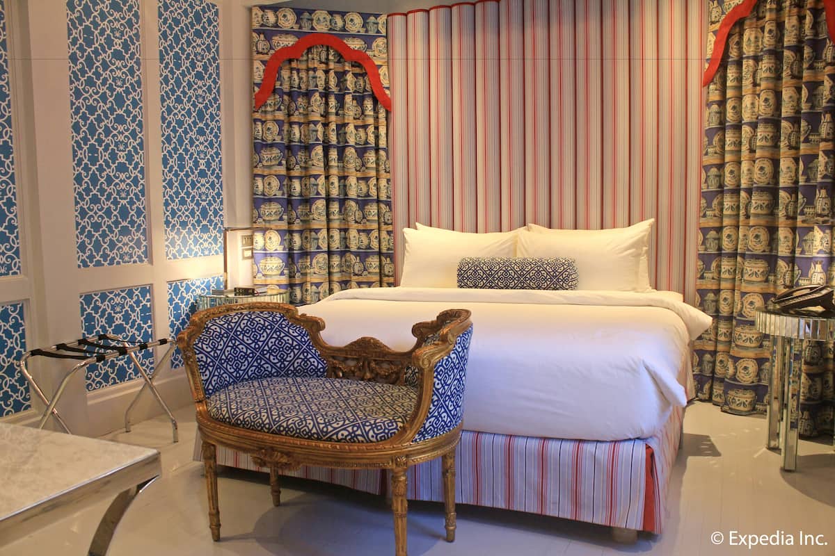 A bedroom with a large bed, a patterned chair, and curtains with a blue and red design.