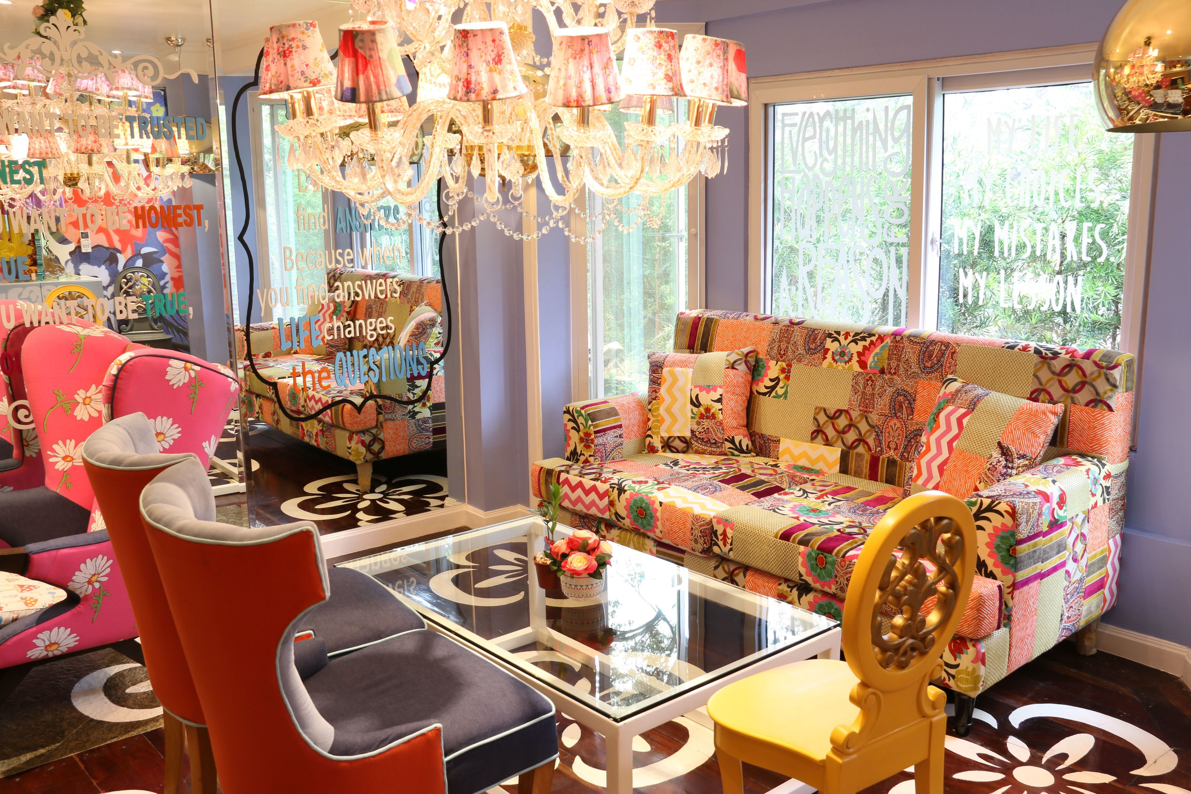 A cozy living room with a colorful sofa, red and blue chairs, a glass coffee table, and a chandelier.