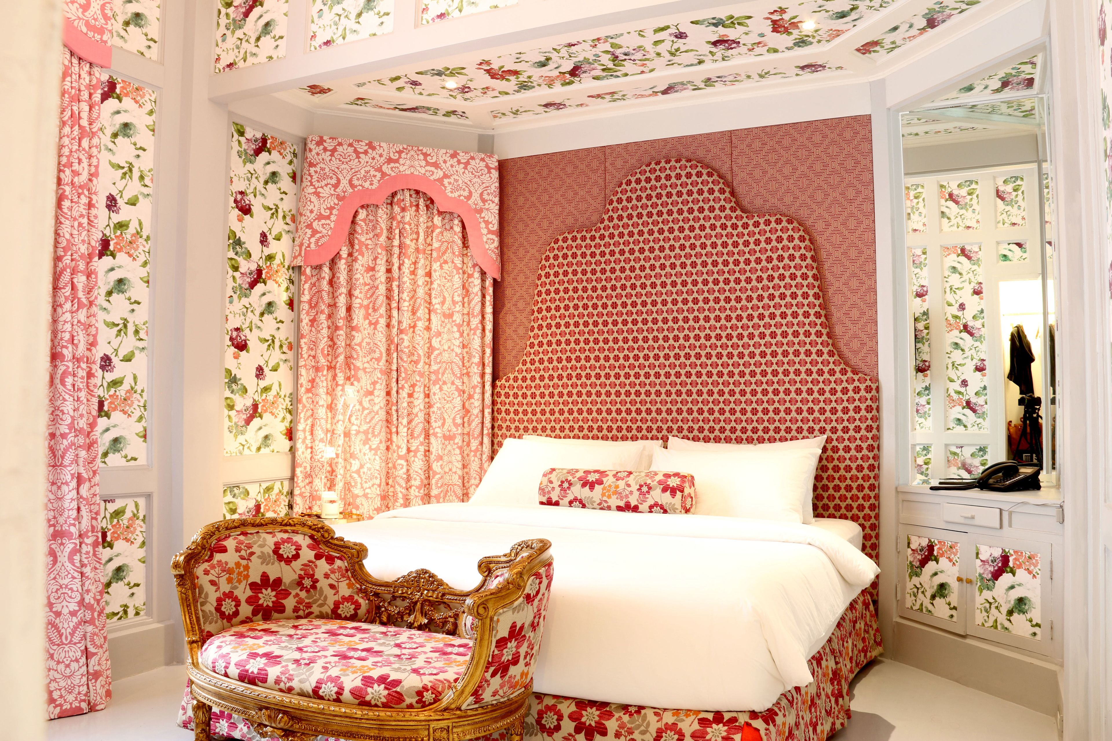 A bedroom with a floral-patterned bed, a matching chair, and a decorative headboard.