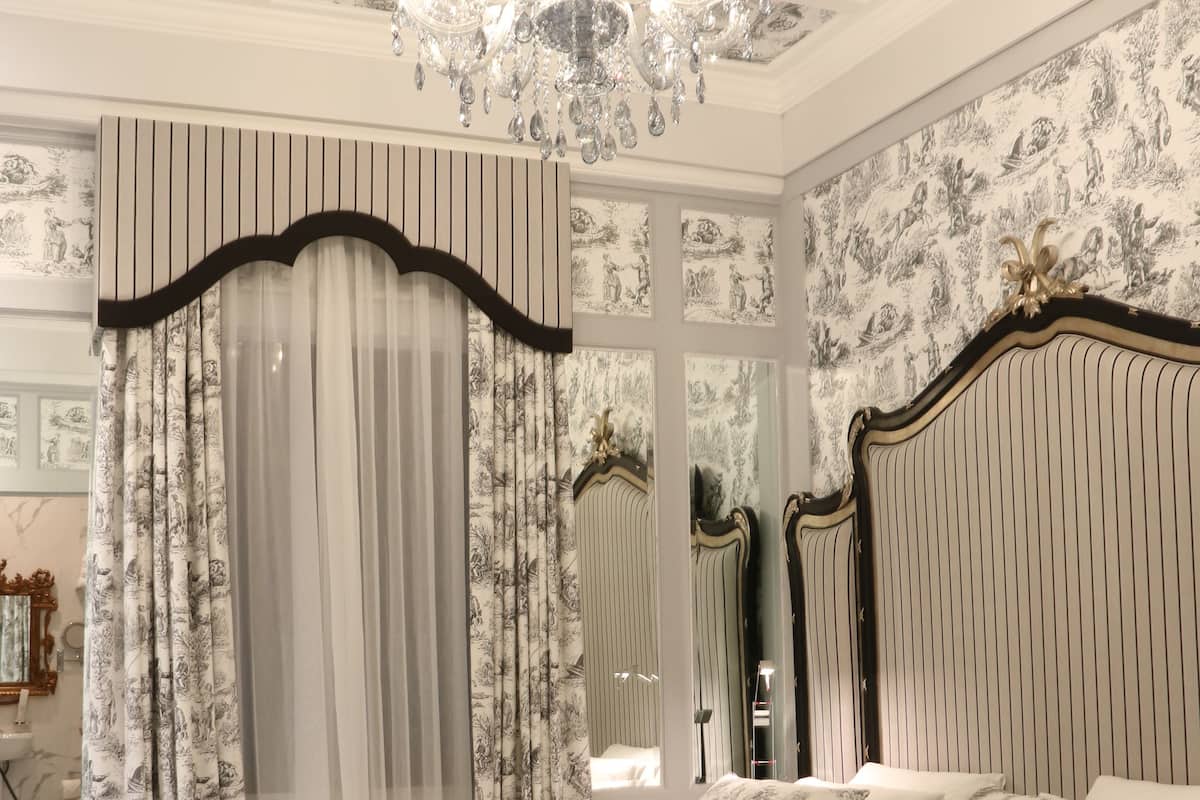 A bedroom with a large bed, a chandelier, and patterned wallpaper.