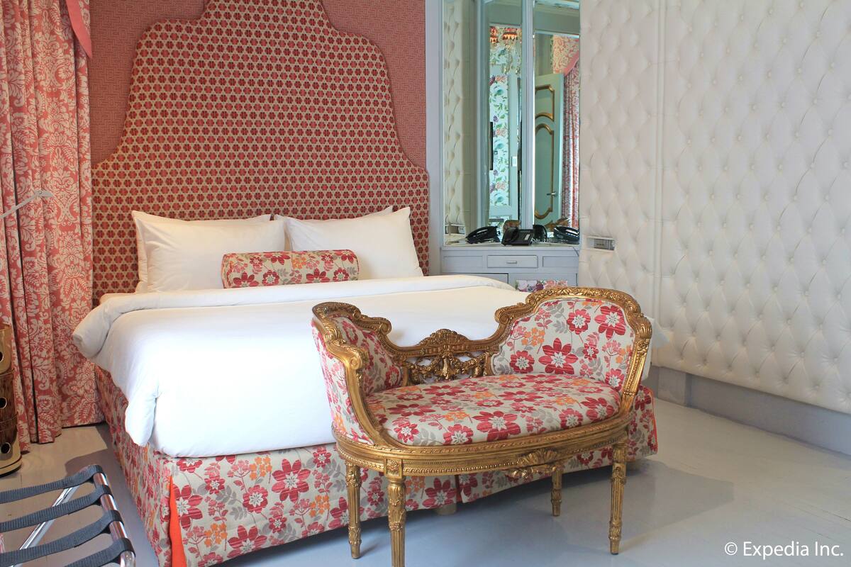 A bedroom with a bed, a chair, a mirror, and patterned walls.