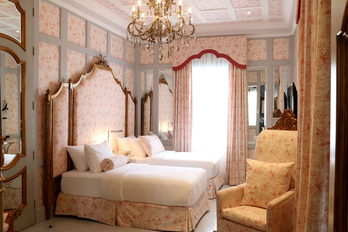A bedroom with two beds, a chandelier, and a chair.