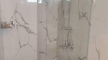 Un baño con ducha de vidrio, inodoro y pared de mármol.