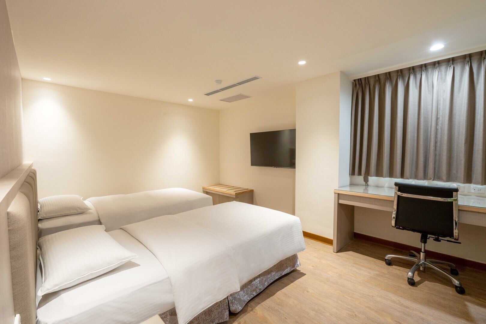Een hotelkamer met een bed, een bureau, een stoel, een televisie en een raam met gordijnen.