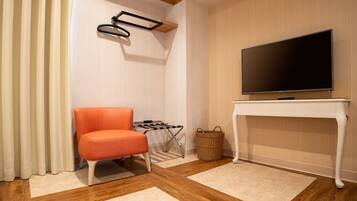 Uma sala de estar moderna com uma TV de tela plana sobre um console branco, uma poltrona laranja, uma pequena mesa lateral e uma cesta de vime.