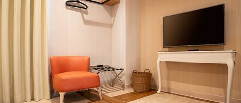 A modern living room with a flat-screen TV on a white console table, a single orange chair, a small side table, and a wicker basket.