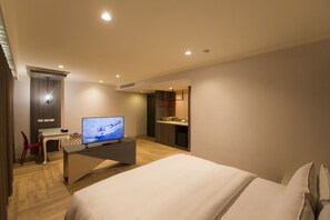 Una habitación de hotel con cama, un escritorio con televisor, una silla y una pequeña kitchenette.