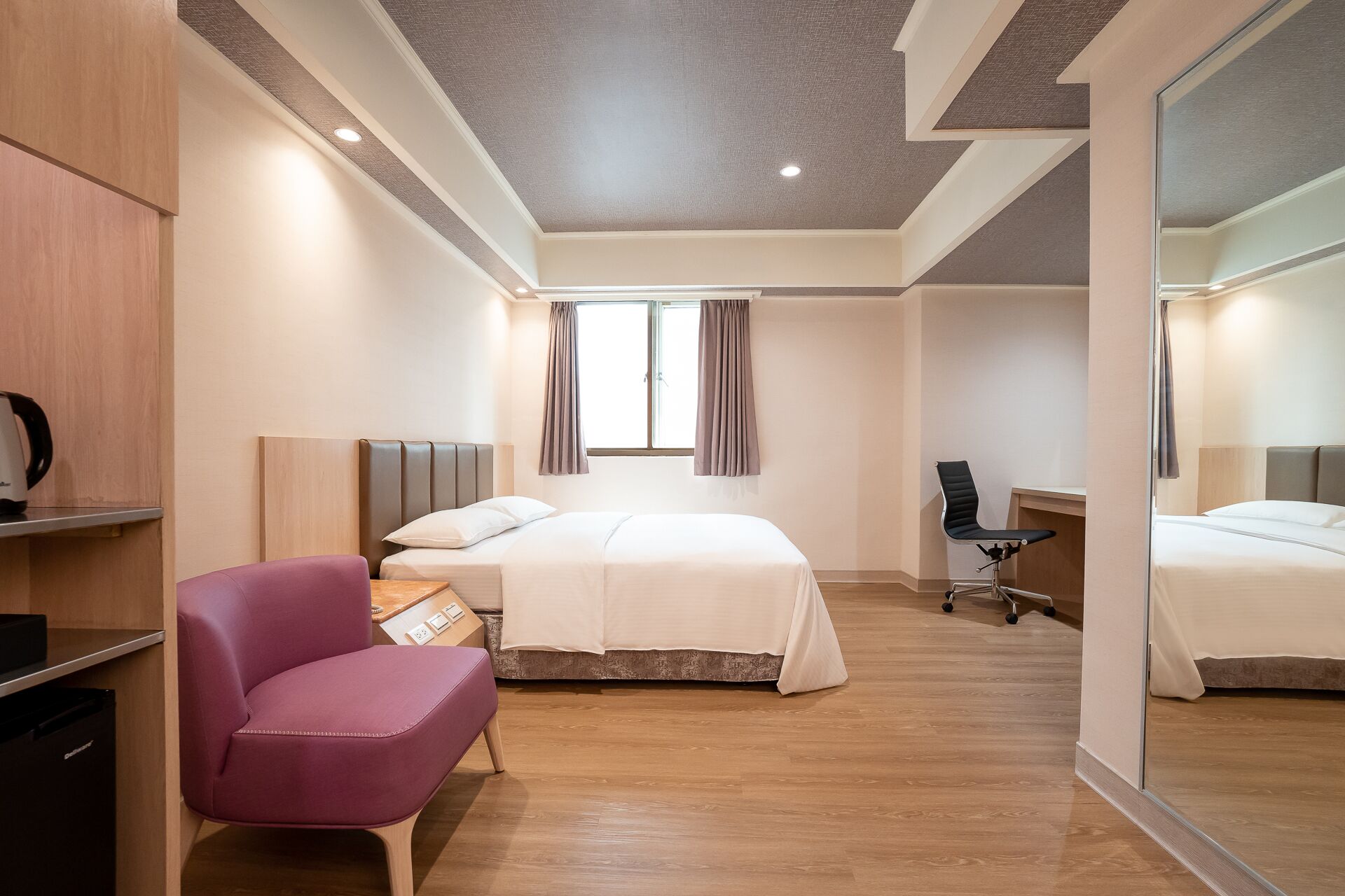 A modern hotel room with a bed, a desk, a chair, and a large mirror.