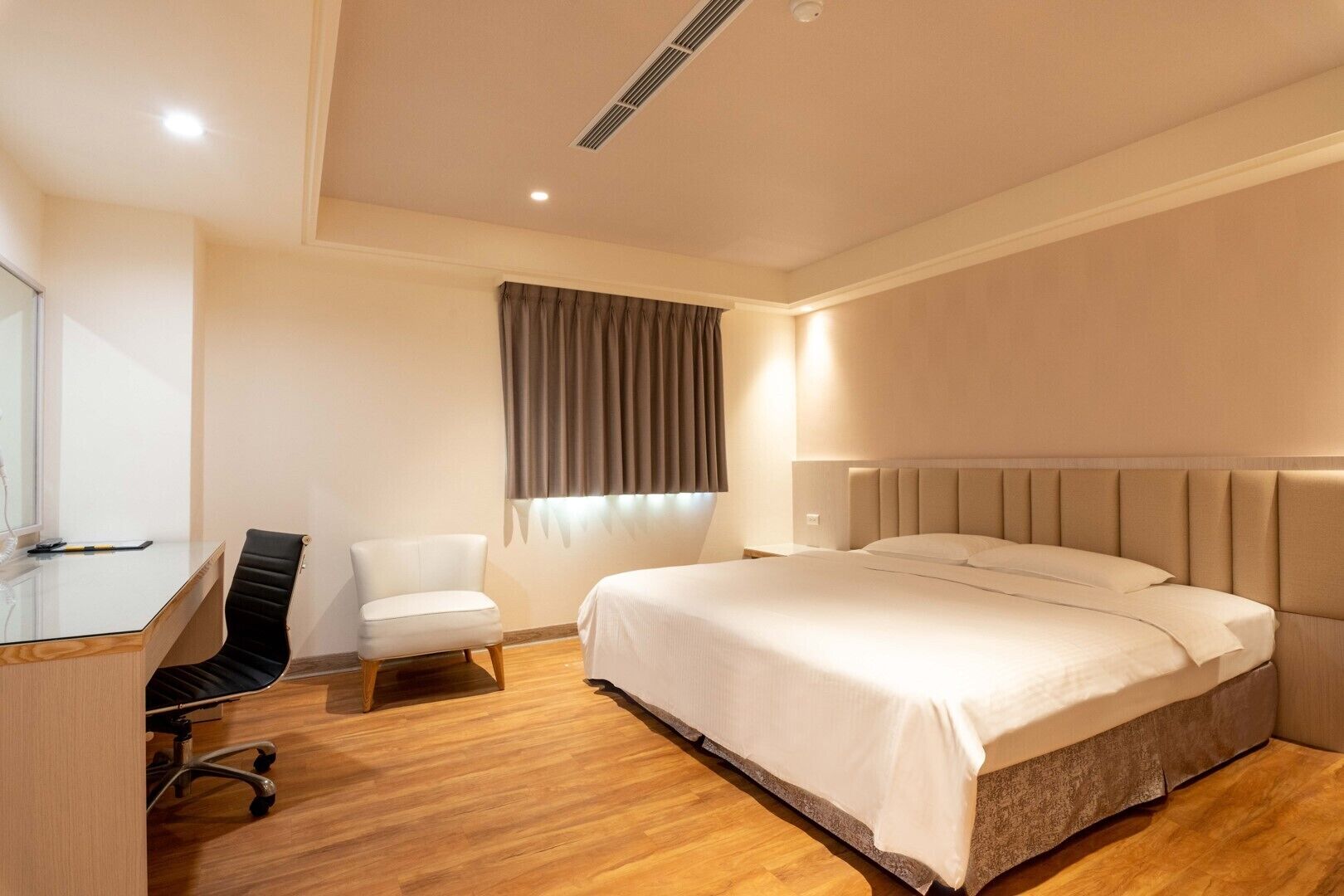 A hotel room with a bed, a desk, a chair, and a window with curtains.