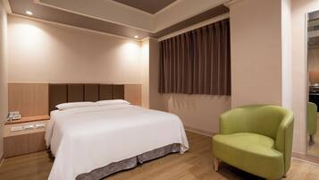 A hotel room with a bed, a green armchair, a bedside table with a phone, and a window with curtains.