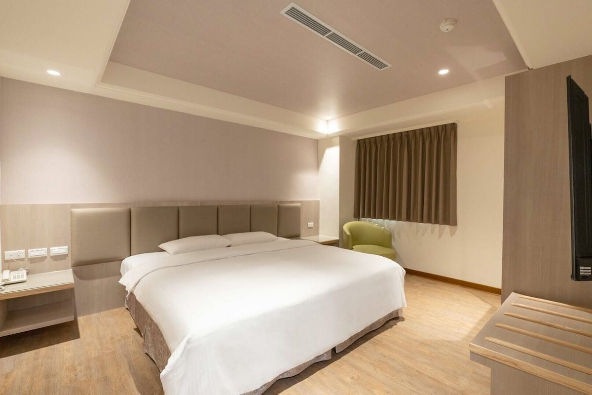 Une chambre d’hôtel moderne avec un grand lit, des tables de chevet, une chaise et un téléviseur.